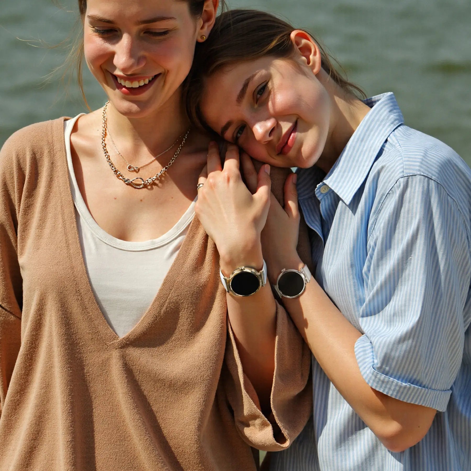 Two women smiling while wearing Runmefit GRACE Smart Watch for Women by a lakeside.